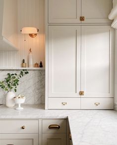 a kitchen with white cabinets and marble counter tops, gold handles and brass pulls on the cupboards