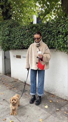 a woman walking her dog on a leash while holding a coffee cup in her hand