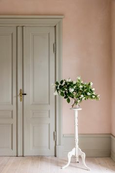 a vase with flowers sitting on top of a white stand in front of a door