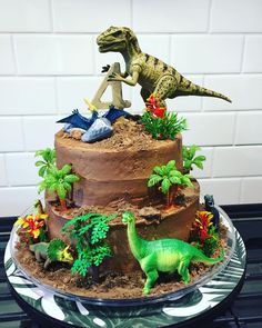 there is a dinosaur cake on top of the table with other dinosaurs and plants around it