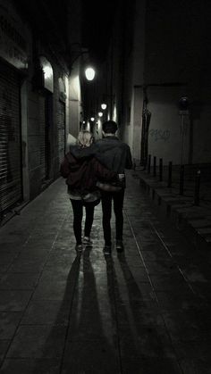 two people are walking down the street at night with their backs to each other,