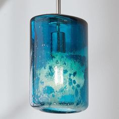 a blue glass light hanging from a metal hook on a white wall with water bubbles in it