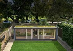 a small house with grass growing on the roof and windows in the back yard, surrounded by greenery