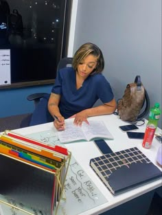 a woman sitting at a desk writing on a piece of paper with several folders next to her