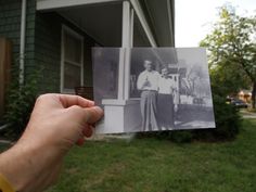 a person holding up an old photo in front of a house