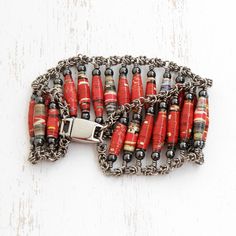 a red and black bracelet with metal chains on top of white wooden table next to bottle opener