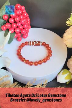 a bracelet with red beads and an omen symbol sits on a table next to flowers