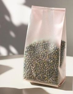 a bag filled with green beans sitting on top of a white table next to a shadow