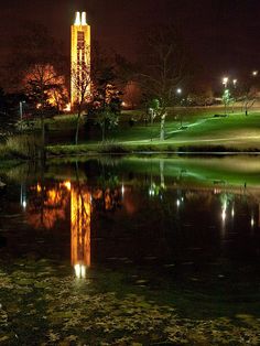 a clock tower is lit up at night by the water's edge with its reflection in the water