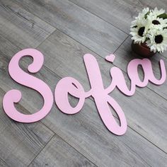 the word sofia is spelled in pink on a wood floor next to a vase with flowers