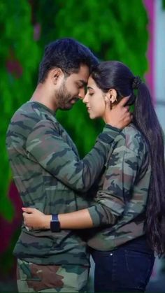 a man and woman embracing each other in front of a green background with trees behind them