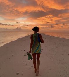 a woman walking on the beach at sunset with her flip flops in front of her