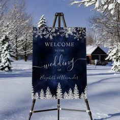 a welcome to the wedding sign in the snow with pine trees and blue sky behind it