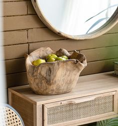 a wooden bowl filled with fruit sitting on top of a table next to a mirror