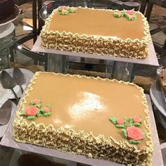 two cakes with frosting and flowers on them sitting on trays in a bakery