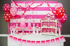 a pink and white birthday party with balloons, cake and decorations on a dresser in front of a striped wall