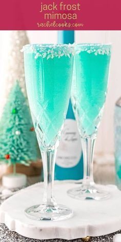 two glasses filled with blue liquid sitting on top of a white tray next to christmas trees