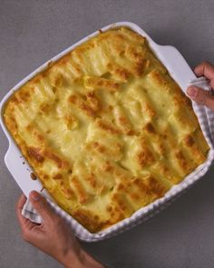 a person holding a casserole dish with cheese on it in front of two hands