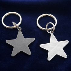 two star shaped key chains sitting on top of a blue velvet surface, one is silver and the other is white