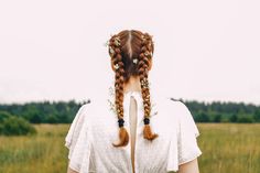 a woman with long red hair standing in a field wearing a white dress and braids