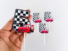 a hand holding a cake topper with cars on it and checkered flags in the background