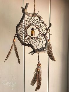 a dream catcher with feathers hanging from it's sides and a bottle in the middle