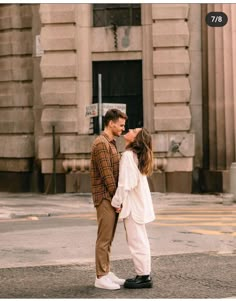 a man and woman standing in front of a building with their noses to each other