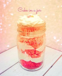 a jar filled with cake in a jar sitting on top of a wooden table next to a pink and white wall