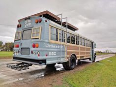 an old school bus is parked on the side of the road in front of a field