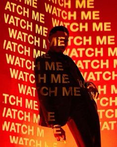 a man standing in front of a red wall with words projected on the wall behind him