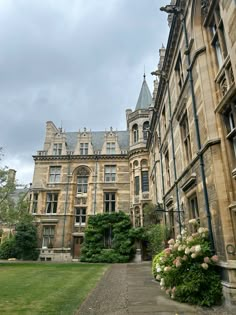 an old building with lots of windows and flowers in the foreground on a cloudy day