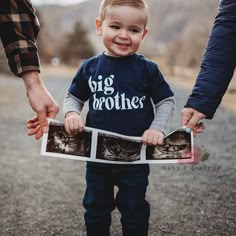 a little boy holding two photos with his parents'hands while walking down the road