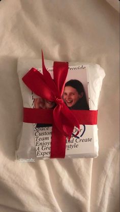 a gift wrapped in white paper with a red ribbon on it's side and an image of a smiling woman