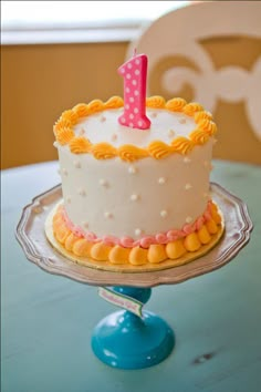 a white cake with yellow icing and a pink number one on top sitting on a table