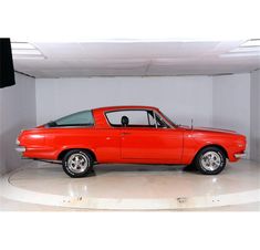 an old red car is parked in a white room with a black floor and ceiling