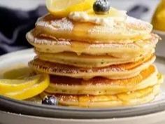 a stack of pancakes topped with blueberries and lemon slices