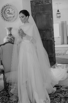 black and white photograph of a woman in a wedding dress standing next to a chair