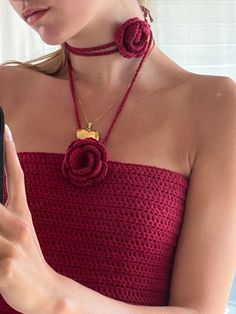 a woman in a red dress holding a cell phone and wearing a necklace with flowers on it