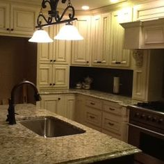 a kitchen with white cabinets and granite counter tops, an island sink and two hanging lights