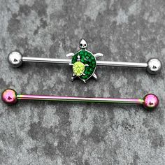 Product Details14 Gauge Green Gem Rainbow Turtle World Industrial Barbell 38mm Set of 2 Keep your options open with this set of 14 gauge helix barbells. The first is made with a 1 1/2 inch 316L surgical grade stainless steel straight barbell with 5mm ball ends. It features a girthy turtle with green gems set into its back. It is carrying a smaller turtle, set with light green gems and you can slide the charm up and down the length of the barbell. You also get one made with a 1 1/2 inch rainbow P Rainbow Turtle, Barbell Earrings, Small Turtles, Green Gem, Industrial Barbell, Lip Ring, Green Gems, Belly Rings, Helix