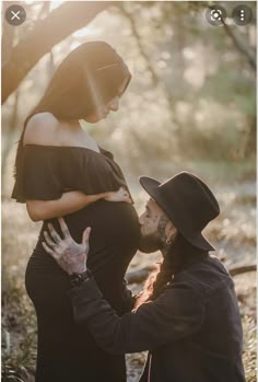 a pregnant woman standing next to a man in a black dress and hat with her hand on the belly