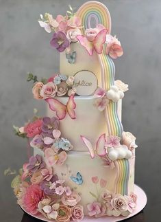 a three tiered cake with flowers and butterflies on the top, decorated in pastel colors