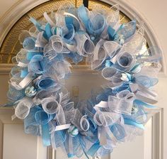 a blue and white mesh wreath hanging on the front door with ribbon around it's edges