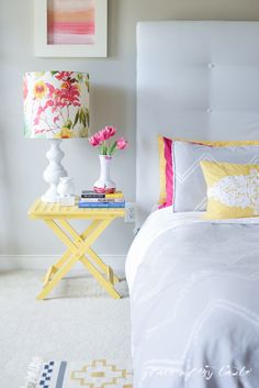 a white bed with yellow and pink pillows on top of it next to a lamp