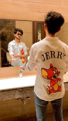 a young man standing in front of a bathroom mirror holding a toothbrush and looking at himself in the mirror