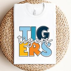 a white t - shirt with the word tigers on it sitting next to a woven basket