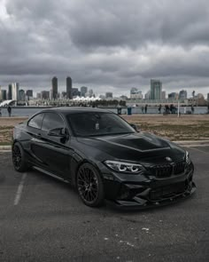 a black bmw car parked in a parking lot with the city skyline behind it on a cloudy day