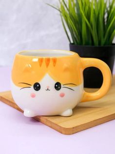 a yellow and white cat mug sitting on top of a wooden tray next to a potted plant