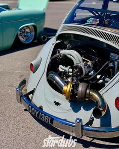 an old vw bug is parked in a parking lot with the hood up open