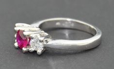 This is a very fine grade Ruby Ring. It is crafted from solid thick Platinum. The ring hold three stones. The center being a very fine grade natural untreated Ruby. It is a round cut and set very securely with four raised prongs. The ruby is of fabulous quality no visible inclusions or abrasions. The color is a deep red with a pink hue. The first two photographs are in natural morning light. The fine stone changes color under different light as you can see from the photographs. On either side of Classic Ruby Ring With Polished Round Stone, Luxury Ruby Three Stone Rings, Classic Three Stone Ruby Ring With Diamonds, Formal White Gold Ruby Ring With Three Stones, Classic Three Stone Round Ruby Ring, Formal Three Stone Emerald Cut Birthstone Ring, Formal Solitaire Ruby Ring With Round Cut, Formal Three-stone Emerald-cut Birthstone Ring, Formal Ruby Three Stone Ring With Diamonds